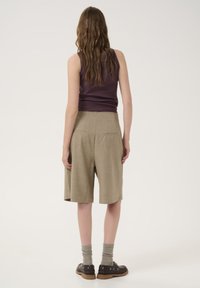 Brown linen shorts with two back pockets, paired with gray knee-length socks and black shoes. The top is a fitted purple sleeveless shirt.