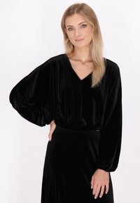 Sort velour top med V-hals og lange, volumin�øse ærmer. Stoffet har en glat overflade, der skaber en subtil glans.