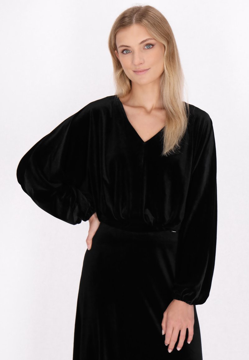 Sort velour top med V-hals og lange, voluminøse ærmer. Stoffet har en glat overflade, der skaber en subtil glans.