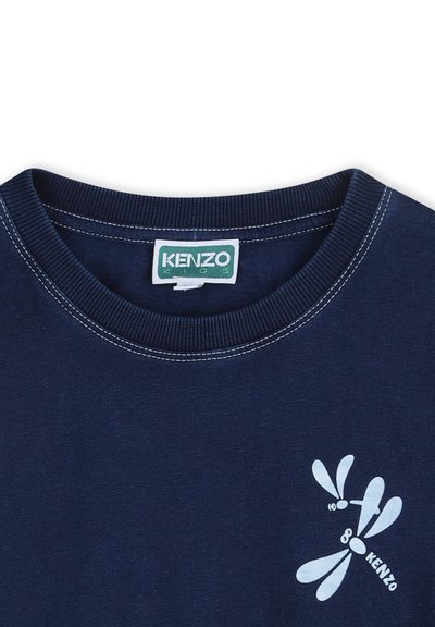 T-shirt en coton bleu marine avec un col ras du cou côtelé, ornée d'un motif libellule blanche et de détails de couture contrastants. Étiquette de la marque visible.