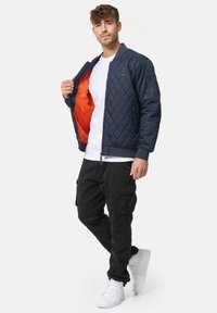 Marineblå quiltet bomberjakke med orange inderside, lynlås lukning, sidelommer, ribbede manchetter, parret med sorte cargo bukser og hvide sneakers.