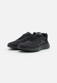 Un paio di scarpe da corsa Adidas nere con tomaia in rete, lacci anteriori e logo del marchio sulla linguetta e sulla suola, mostrato su sfondo bianco.