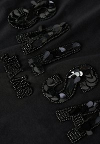 Tela negra con lentejuelas y cuentas negras brillantes dispuestas en patrones decorativos de texto. Enfoque en la textura y en los detalles de los embellishments.