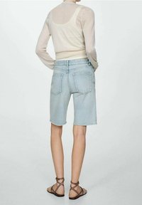 Světle modré džínové šortky s třepícími se okraji, se zadními kapsami a středním pasem, v kombinaci s poloprůhledným béžovým topem a sandály.