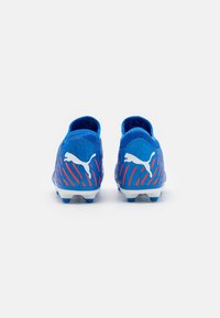 Scarpini da calcio blu con superficie testurizzata, caratterizzati da strisce diagonali rosse e loghi bianchi Puma sul tallone. Tacchetti in gomma resistente sulla suola.