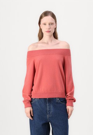 Maglione a spalla scoperta in maglia corallo con maniche lunghe e orlo a costine, abbinato a jeans in denim blu a vita alta. Texture morbida, vestibilità casual.