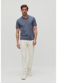 Miestenska polokošeľa tmavomodrej farby s krátkymi rukávmi, skombinovaná s krémovými slim-fit nohavicami a bielymi teniskami. Jednoduchý, neformálny dizajn.