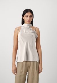 Top senza maniche color beige chiaro con un alto colletto arruffato, caratterizzato da una superficie liscia in satin e un design asimmetrico su un lato.