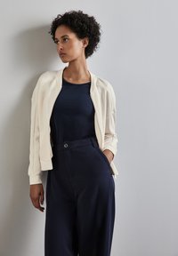 Una chaqueta bomber de crema clara sobre una camiseta navy, combinada con pantalones de tiro alto en color navy. Tejido suave con un corte relajado y detalles de diseño mínimos.