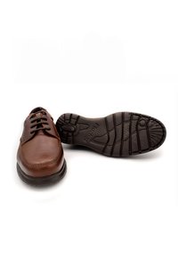 Zapatos de cuero marrón con cordones, con una superficie lisa, punta redonda y suela de goma negra texturizada con patrones distintivos.