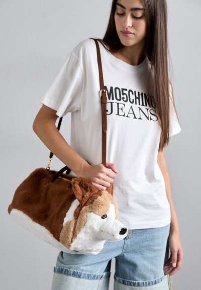 Femme portant un t-shirt blanc Moschino Jeans et un short en denim tient un sac à main en peluche en forme de chien brun et blanc avec une bandoulière en cuir.