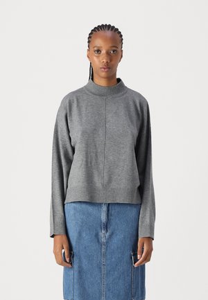 Pull en tricot gris avec un col montant, des manches longues et un ourlet côtelé, associé à une jupe en jean bleu avec deux poches latérales.