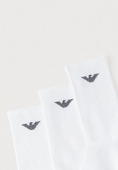 Hvide bomuldssokker med ribbet tekstur, med en sort logo nær toppen. Tre par vist jævnt fordelt.