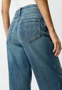Jeans de mezclilla azul de pierna ancha con cintura alta, que cuentan con dos bolsillos traseros de parche y detalles de costura visibles. Textura suave con un acabado desgastado.