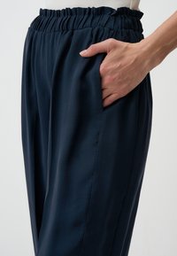 Navyblaue Hose mit einem gerafften elastischen Bund, seitlichen Taschen und einer glatten Textur. Sie bietet einen lockeren Schnitt und klare Linien.