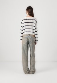 Suéter de estilo crochet con rayas horizontales en color marino sobre una base blanca y jeans de tiro alto en un lavado claro con un ajuste relajado y bolsillos.
