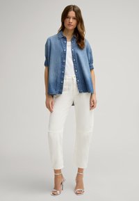 Denim shirt in blue, buttoned with rolled sleeves, paired with white cropped trousers featuring patch details and silver heeled sandals.