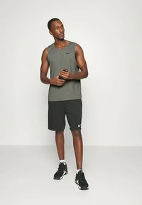 Herre treningsoutfit: grå ermeløs topp, svarte shorts med hvit Nike-logo, iført svart og hvit sneakers, stående i en nøytral setting.