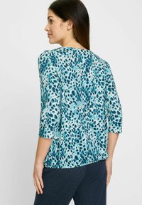 Kurzarmpullover in Hellblau mit einem Farbspritzmuster in Dunkelblau und Türkis. Glattes Material mit einer lockeren Passform und Rundhalsausschnitt.