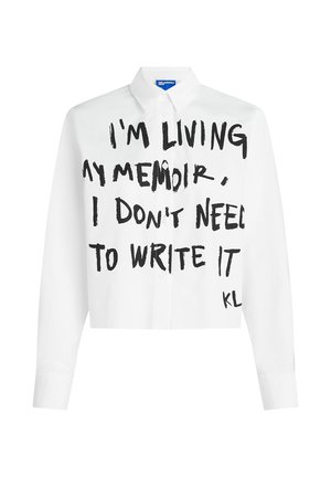 Camisa blanca recortada de botones con texto manuscrito en negro: "VIVO MI MEMORIA, NO NECESITO ESCRIBIRLA," firmada "KL". Tela de algodón puro.