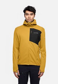 Gele softshell jas met een zwart borstzakje, ritssluiting en verstelbare capuchon. Heeft een gestroomlijnd, aansluitend ontwerp en een gestructureerde stof.