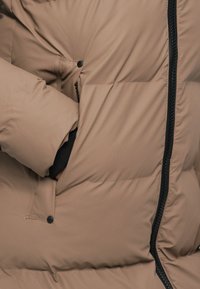 Brązowa kurtka puchowa z zamkiem błyskawicznym z przodu, teksturowanym materiałem i kieszenią boczną z zapięciem na napy.