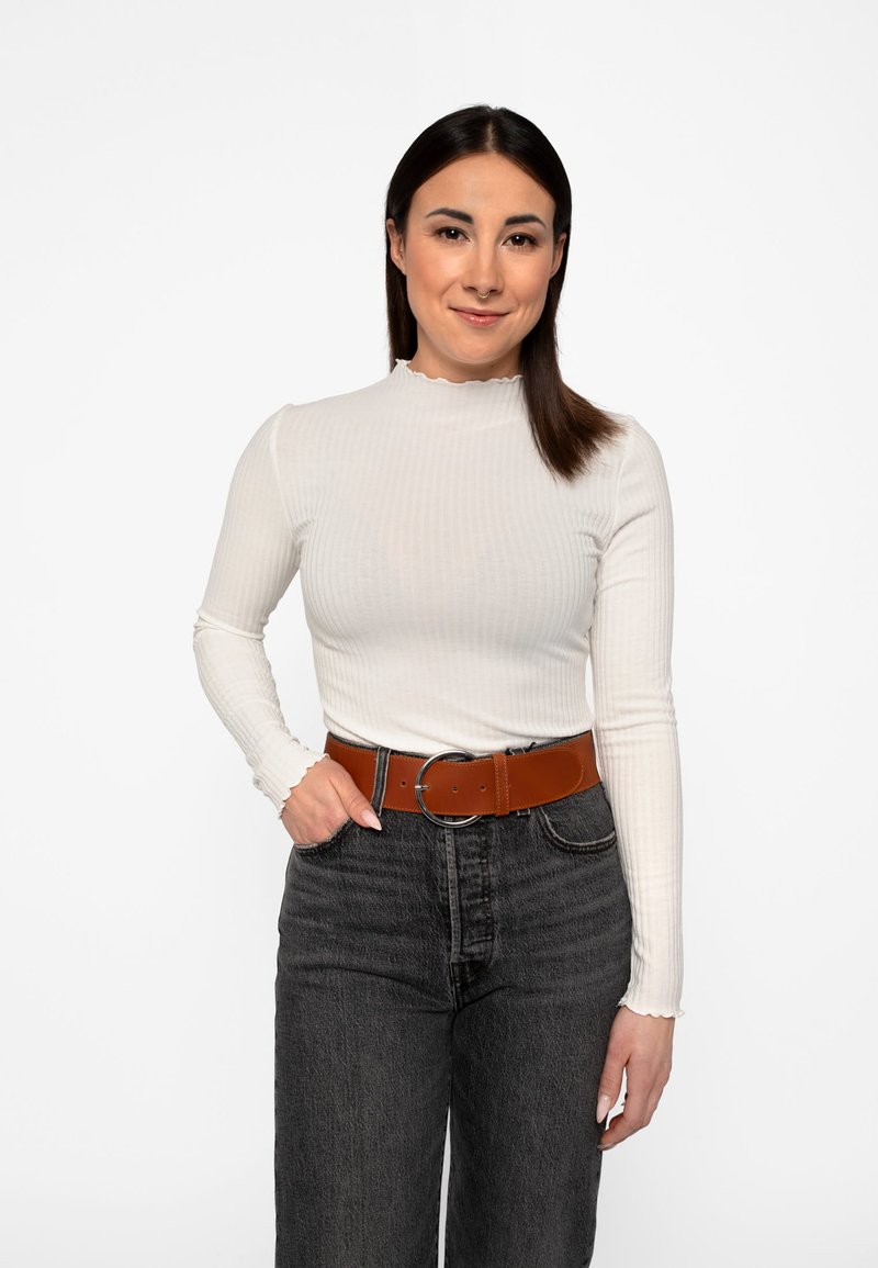 Hvid ribbet langærmet top med en bølget halsudskæring, parret med højtaljede mørkegrå jeans og et brunt læderbælte med en rund spænde.