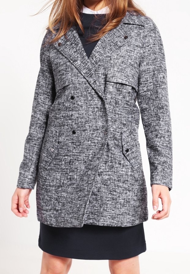 Cappotto grigio strutturato doppiopetto con rever a punta, due tasche laterali e bottoni neri. Indossato sopra un vestito scuro. Finitura in tessuto liscia.