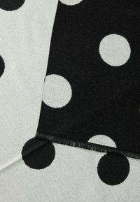 Must-valge mustriga kangas, millel on suured kontrastsed täpid. Pehme tekstuur, sasitud servade ja geomeetrilise kujundusega.