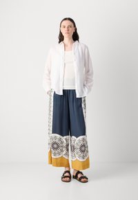 White linen button-up shirt, white tank top, navy patterned wide-leg pants with yellow accents, and black sandals. Smooth texture, relaxed fit.