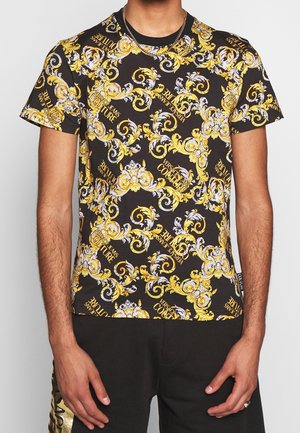 Camiseta negra con un patrón barroco en oro y blanco y el texto "Versace Jeans Couture" en fuente negrita repetida. Manga corta y cuello redondo.