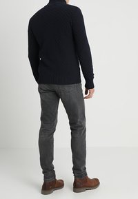 Marinblått stickat tröja med hög krage, ihopparad med slim-fit mörkgrå jeans och bruna läderstövlar. Strukturerad tyg med ribbade detaljer.