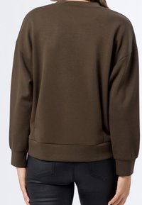 Brun sweatshirt med avslappnad passform, långa ärmar och rundad halsringning. Slätt, elastiskt tyg med ribbade muddarna och fållen.