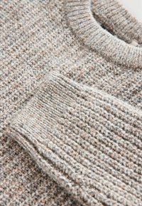 Maglione lavorato a maglia grigio e beige con scollo rotondo e polsini a coste, che mette in evidenza un tessuto caldo e morbido con un motivo sottile.