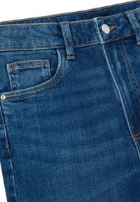 Primo piano dei pantaloni in denim blu con bottone, passanti per cintura e dettagli della cucitura della tasca anteriore.