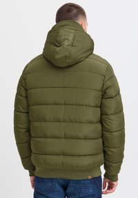 Olivgrüne Pufferjacke mit einer Kordelzugkapuze, gestepptem Design und geripptem Saum. Strukturiert, mit glatter Oberfläche und sichtbaren Nähten.
