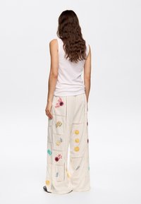 Bestickte cremefarbene weite Hose mit bunten Blumenmustern und Spitzenbesatz, kombiniert mit einem schlichten ärmellosen Oberteil.