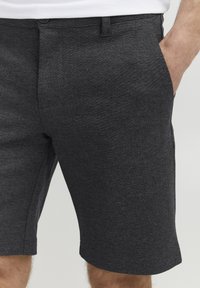 Shorts gris en tissu texturé, avec une taille plate, des poches latérales et un ourlet propre. Détails de bouton et de passants de ceinture visibles.