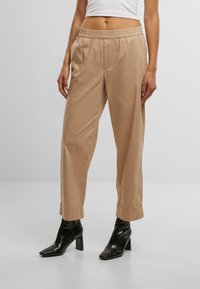 Pantaloni beige leggeri con design affusolato, vita elastica e orli arrotolati. Indossati con stivaletti neri con tacco.