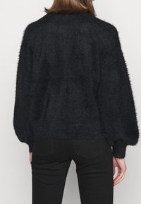 Pull noir texturé avec une finition duveteuse. Présente une coupe décontractée, des manches ballon et un ourlet côtelé. Porté avec un pantalon noir.