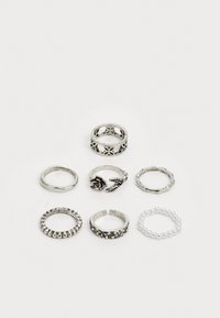 Sept bagues en argent de designs variés : accents floraux et de feuilles détaillés, bandes lisses, texture perlée, et une avec de petites perles.