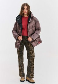 Puchowa kurtka w ciemnym brązie z czarnym kapturem, noszona na czerwonym topie i spodniach w panterkę. Botki z beżowego materiału z czarnymi podeszwami.