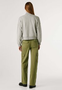Sudadera gris con cuello alto, combinada con pantalones cargo verde oliva que tienen múltiples bolsillos. Unos zapatos negros completan el conjunto.