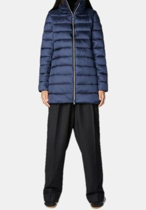 Personne portant une doudoune matelassée bleu marine avec une fermeture éclair frontale et un pantalon large noir, sur un fond uni.