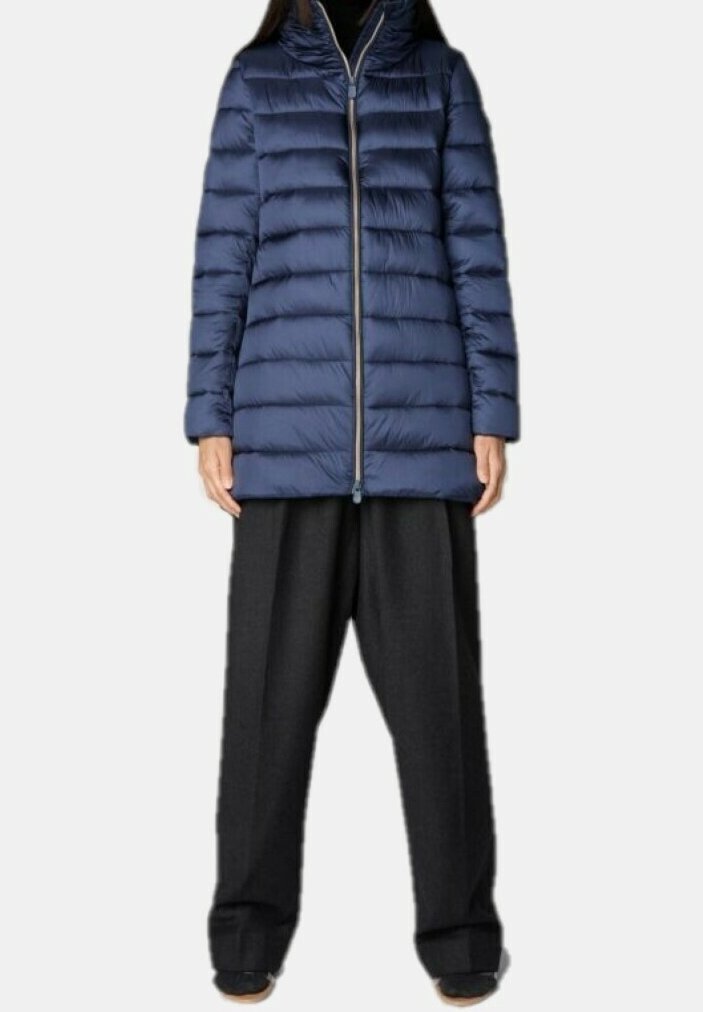 Personne portant une doudoune matelassée bleu marine avec une fermeture éclair frontale et un pantalon large noir, sur un fond uni.