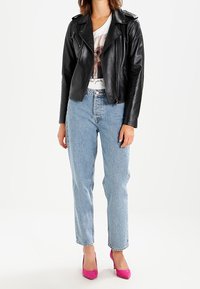 Chaqueta de cuero negra de motorista con cremalleras, camiseta gráfica blanca, jeans de cintura alta azul claro y tacones rosas. Atuendo casual.