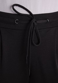 Svart dragsko i midjan med två metallöglor och en texturerad tyg. Dragsnöret har ändar med aglets för enkel justering.