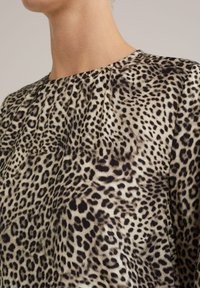 Topp med leopardmönster i en texturerad tyg, rund halsringning och plisserad design i nyanser av beige och svart.
