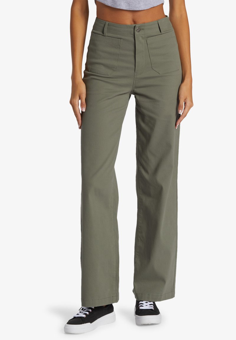 Olijfgroene wijde broek van katoen-twill, met een hoge taille, zijzakken en een knoopsluiting, gedragen met zwarte sneakers.
