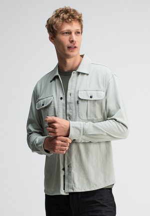 Lichtgroene button-up shirt met twee borstzakken, lange mouwen en een rechte snit; gemaakt van een zachte stof met een gladde textuur.